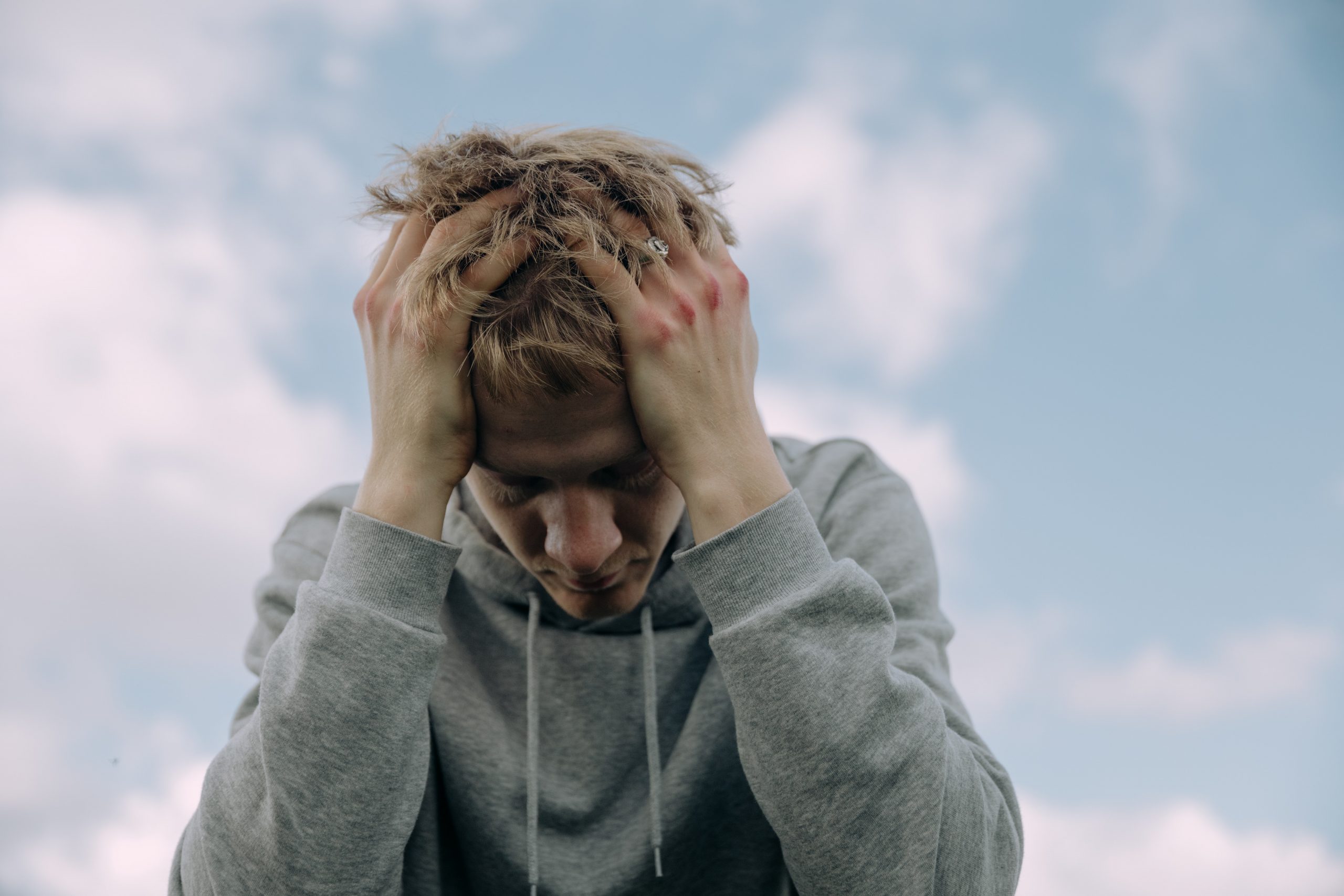 Young man with hands in his hair looking down and depressed