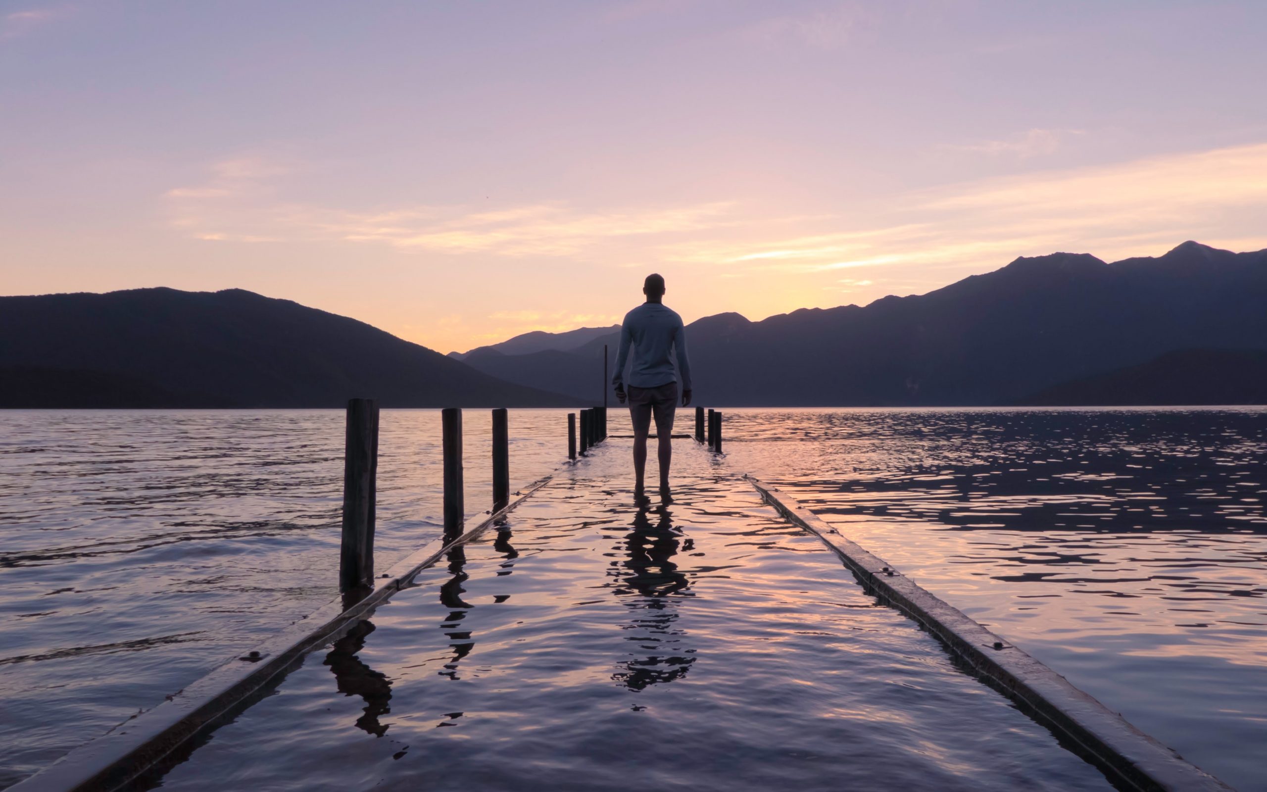 Man standing alone on pier watching sunrise